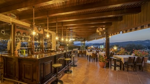 Zona de bar al aire libre con techo de madera, lámparas colgantes y vistas a la ciudad.
