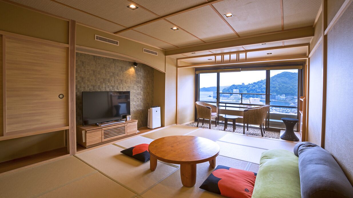 Ein traditionelles japanisches Wohnzimmer mit Tatami-Böden, einem Fernseher, einem runden Tisch und Blick auf eine Berglandschaft.