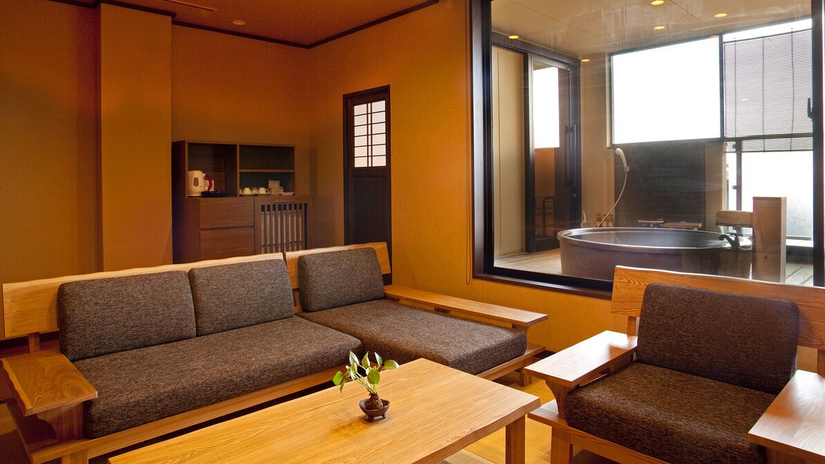 Un interior moderno con un sofá, sillas, una mesa de madera y vistas a un jacuzzi a través de un ventanal grande.