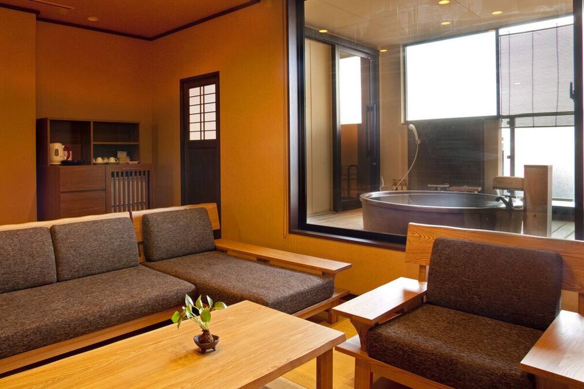 A modern interior with a sofa, chairs, a wooden table, and a view of a hot tub through a large window.