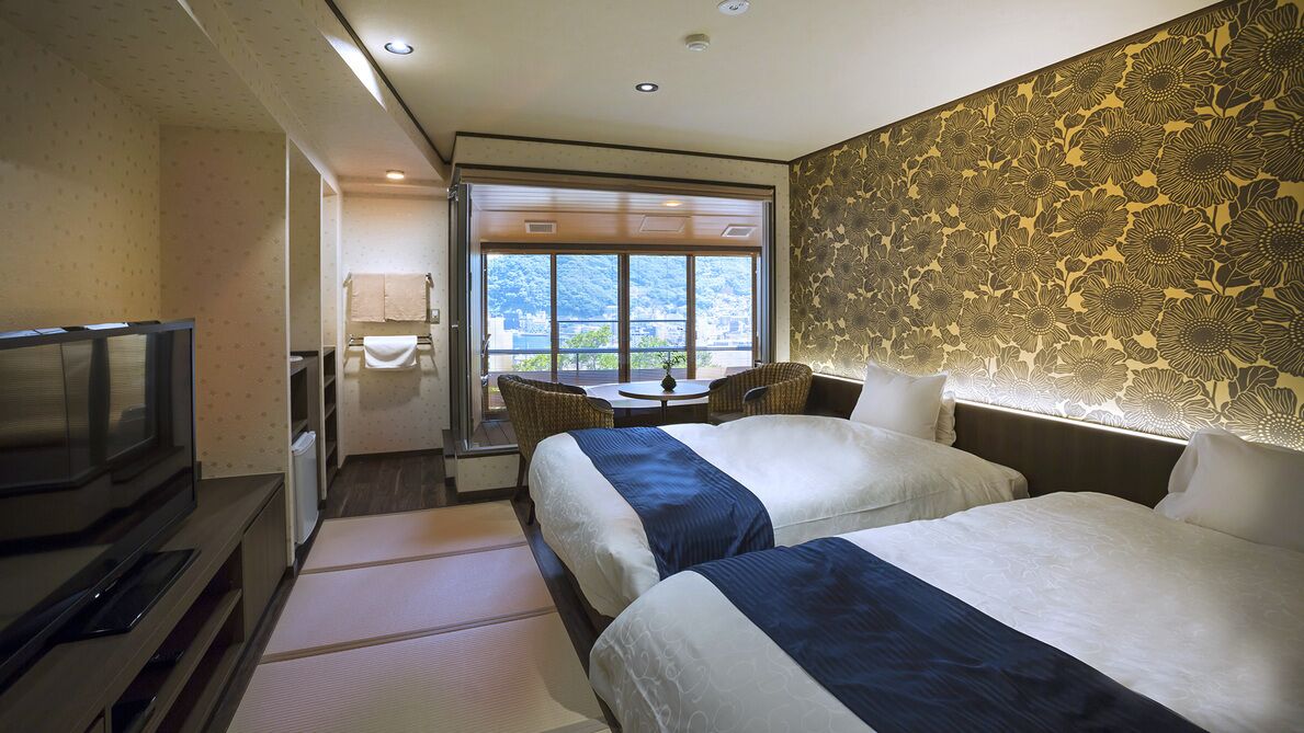 Ein Hotelzimmer mit zwei Betten, einem Fernseher, einem kleinen Tisch und Blick ins Freie.
