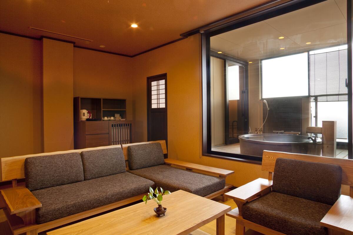 A modern interior with a sofa, a wooden table, and a view of a hot tub through a large window.
