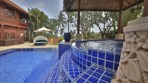 A swimming pool with blue tiles, a lounge area with a white umbrella, and a stone sculpture.