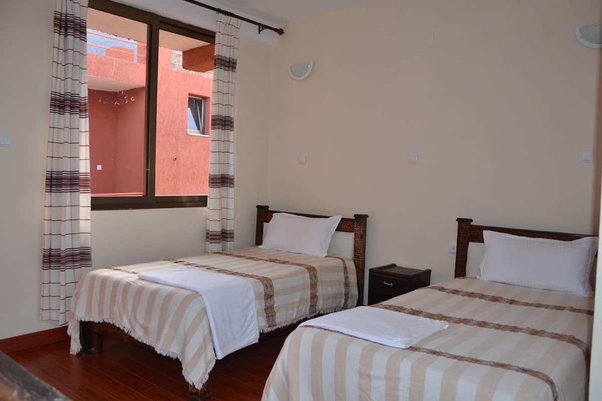 A bedroom with two beds, a window with curtains, and a view of a red building outside.