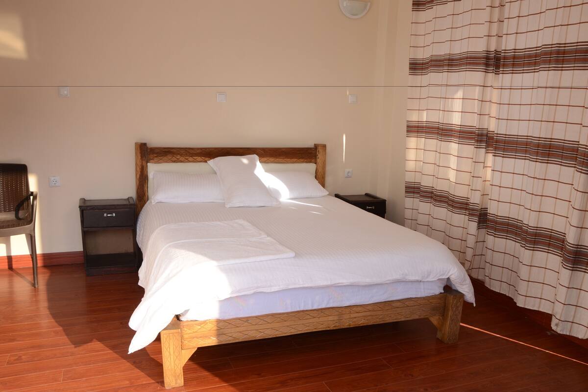 A neatly made bed with white linens, a wooden headboard, and a nightstand with a lamp.
