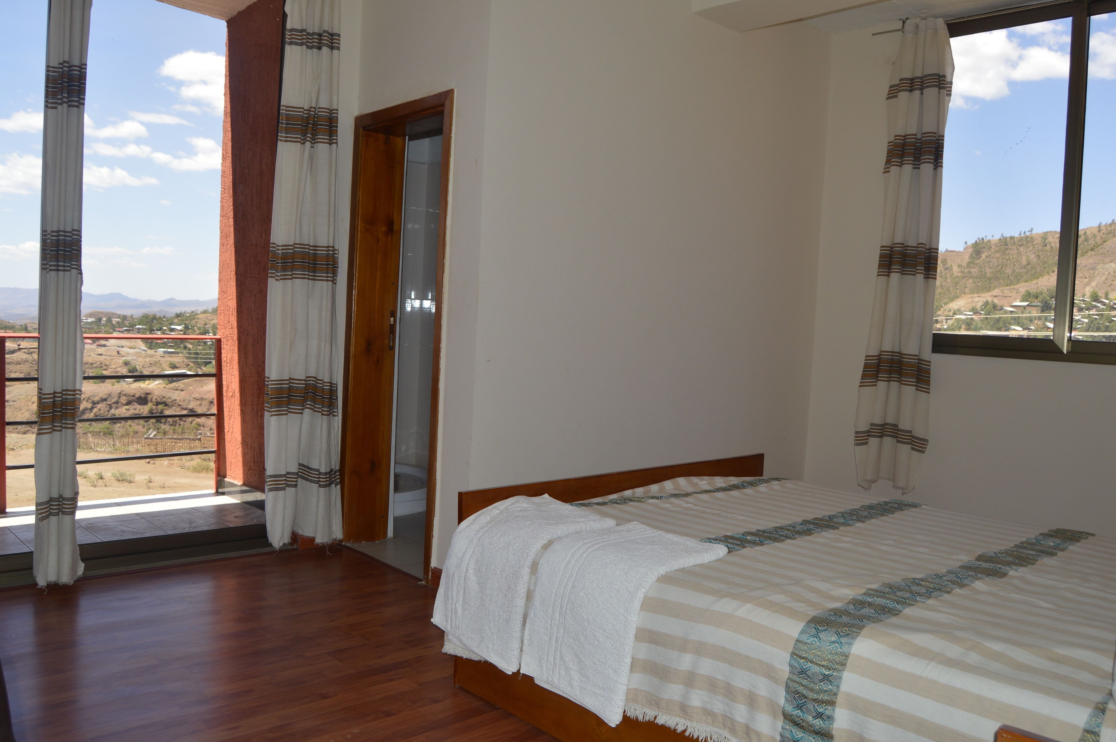 Un dormitorio con cama de madera, cortinas blancas y vistas a un paisaje montañoso.