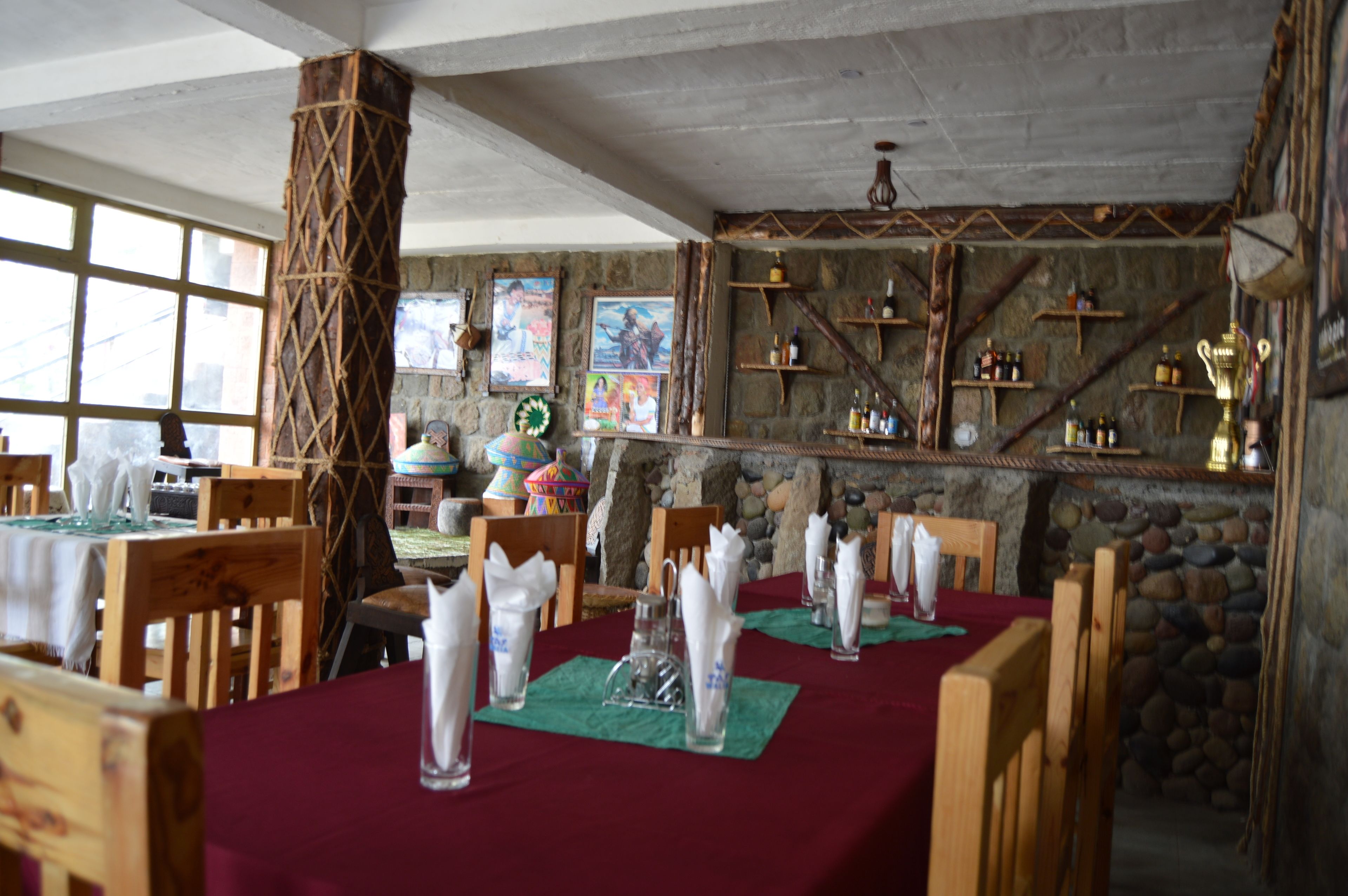 Un restaurant avec des tables en bois, nappées de serviettes blanches et agrémentées de verres, des murs en pierre et des étagères remplies de bouteilles.