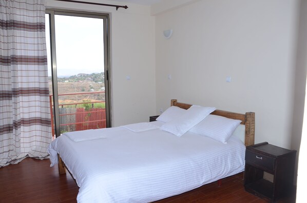 A bedroom with a large bed, a wooden headboard, a nightstand, and a view through a sliding glass door. - Zan-Seyoum Hotel (Lalibela)