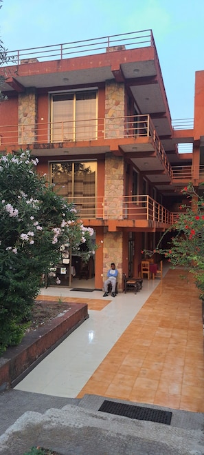A modern building with a stone facade, a covered outdoor seating area, and a person sitting on a bench. - Zan-Seyoum Hotel (Lalibela)