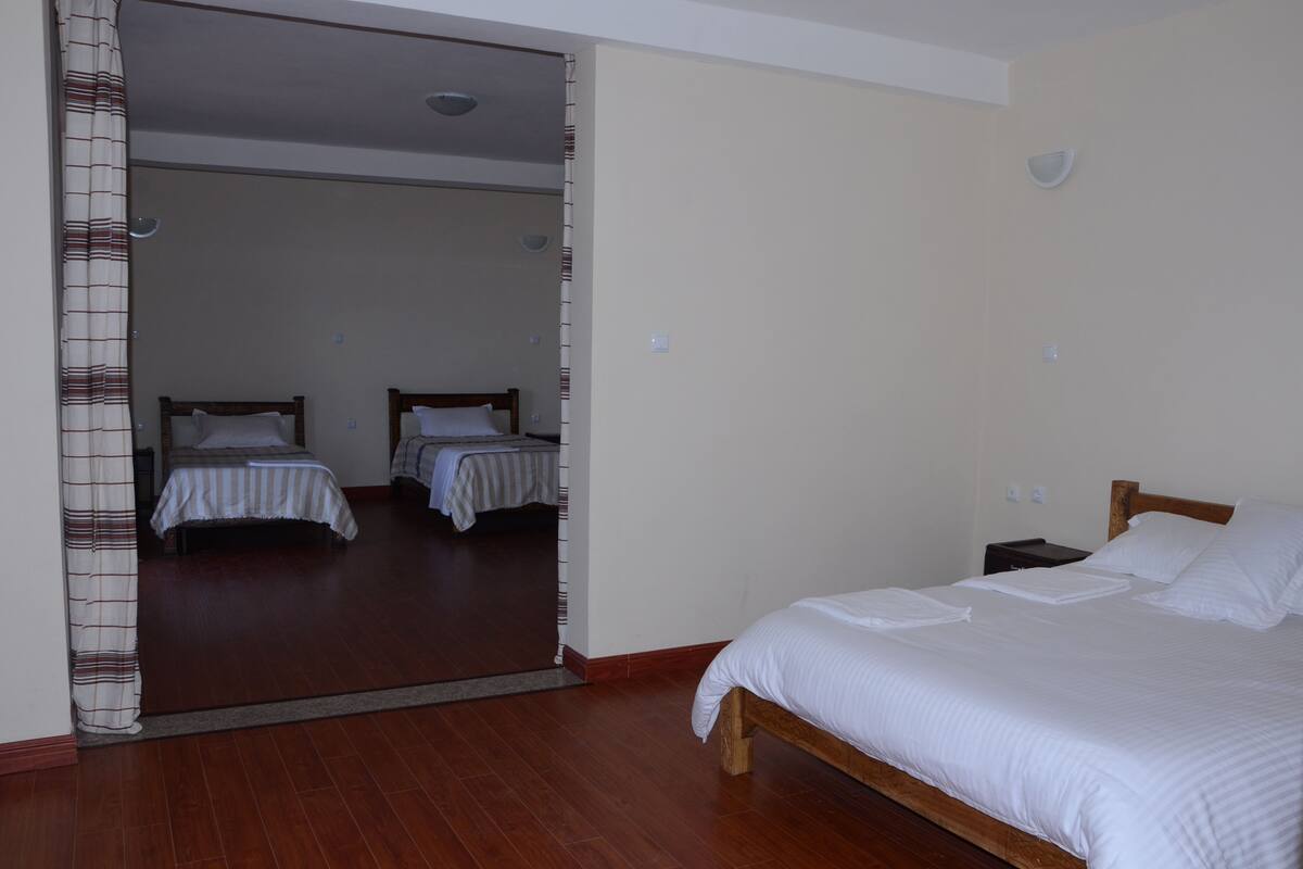 A hotel room with a wooden bed, a mirror, and two smaller beds in the background.