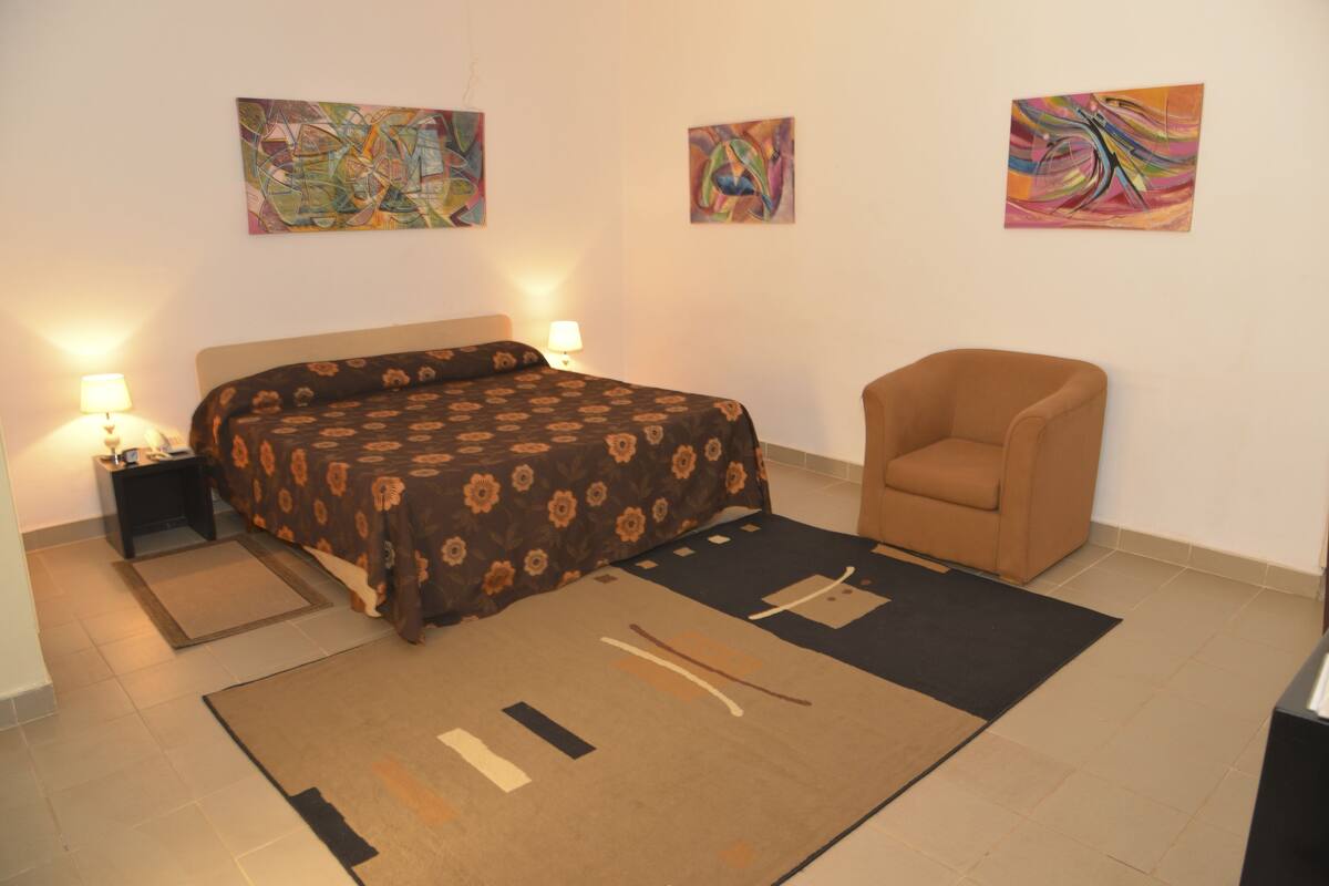 Un dormitorio con cama, una silla y arte abstracto en las paredes.