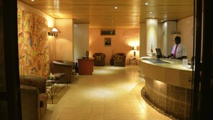 A reception area with a wooden ceiling, a reception desk, a counter, and two armchairs. - Hotel La Coccinelle (Bamako)