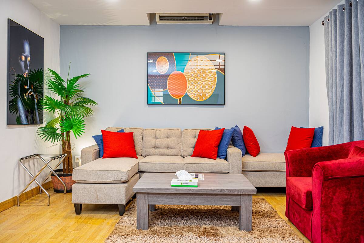 Una sala de estar con un sofá modular, un sillón rojo, una mesa de centro y un cuadro abstracto de gran tamaño en la pared.