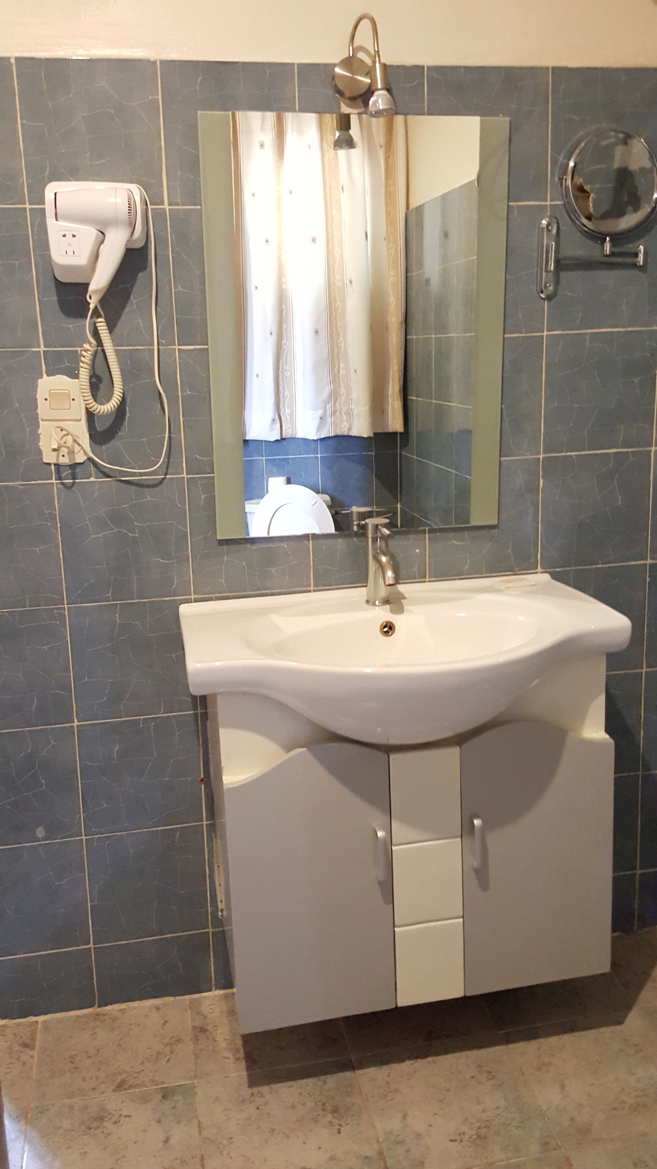 Un bagno con un lavandino bianco, uno specchio e un portascopevoli.