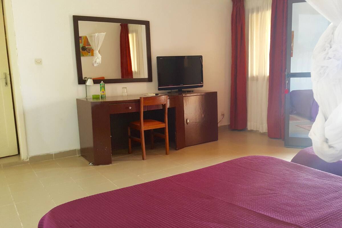 Una habitación de hotel con una cama, un escritorio con silla, un televisor y una ventana con cortinas.