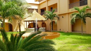 A courtyard with a central water feature, palm trees, and a building with balconies. - Hotel La Coccinelle (Bamako)
