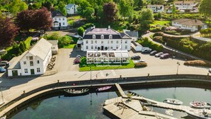 A large white building with a central courtyard, surrounded by greenery and a body of water with boats. - Bekkjarvik Gjestgiveri | Beckerwyc House (Austevoll)