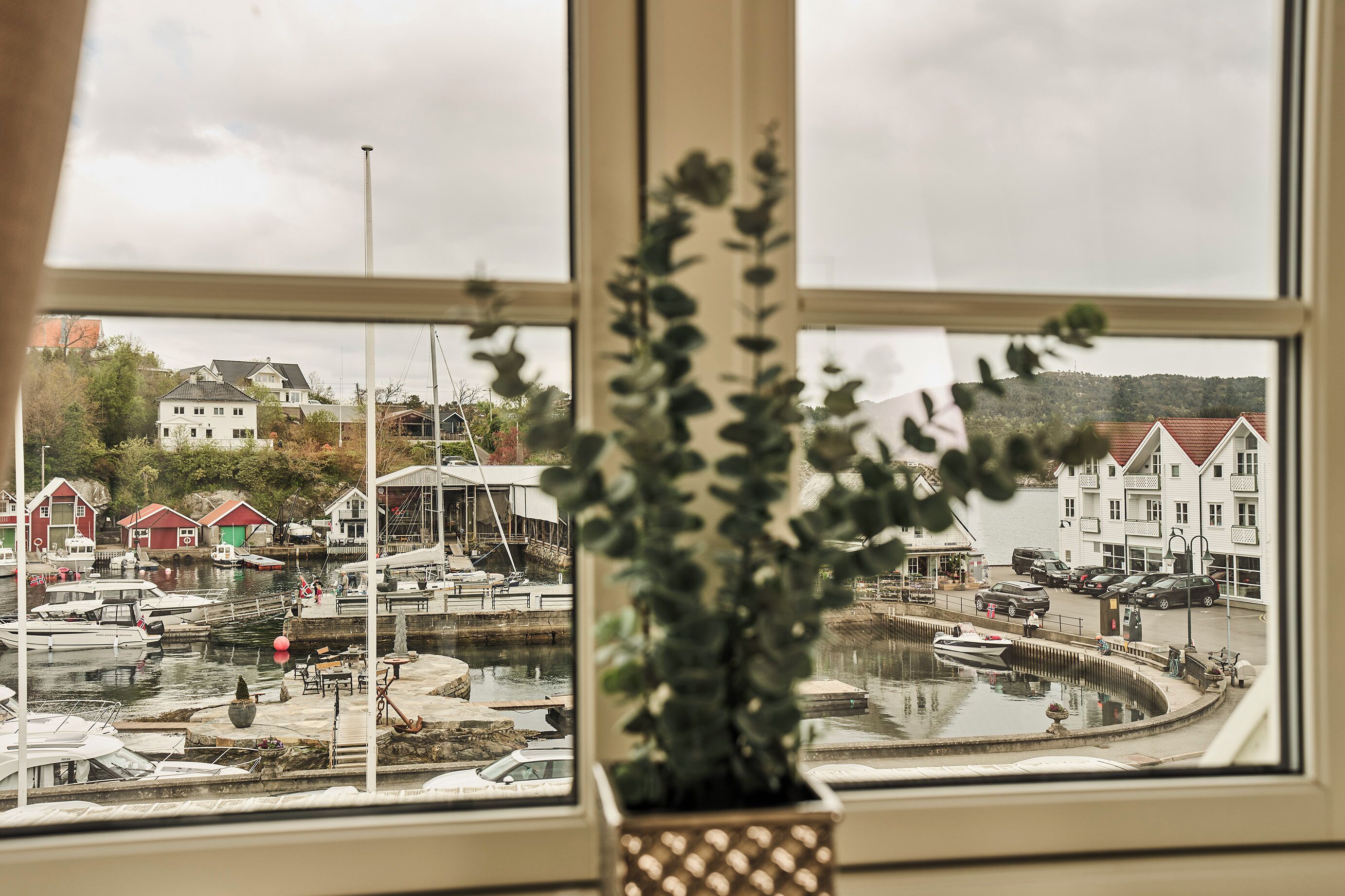 Blick auf einen Yachthafen mit vertäuten Booten, ein Gebäude mit rotem Dach und eine Hügelkulisse im Hintergrund.