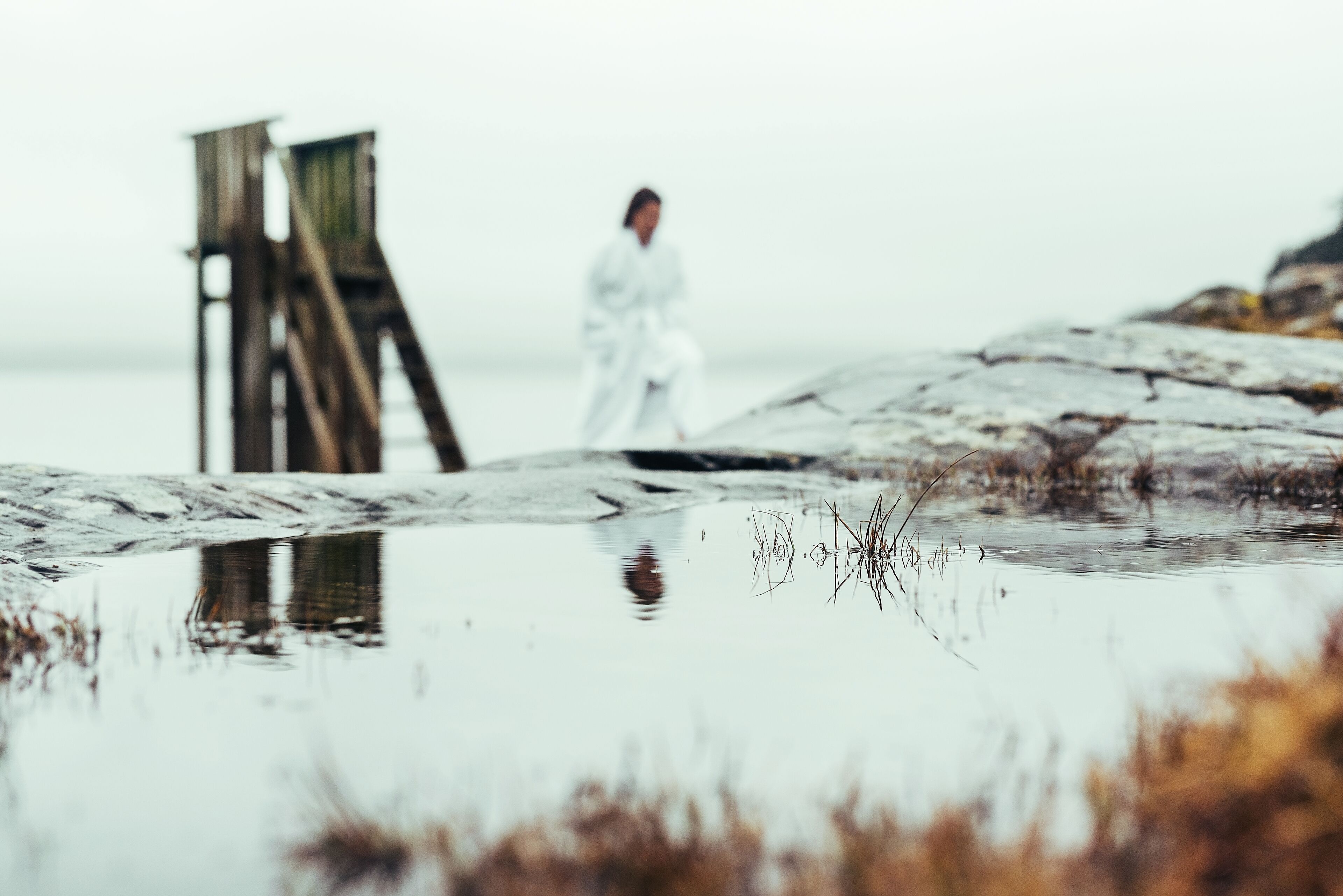 Une jetée en bois s’étendant dans une étendue d’eau, sur laquelle une personne vêtue de blanc s’éloigne.