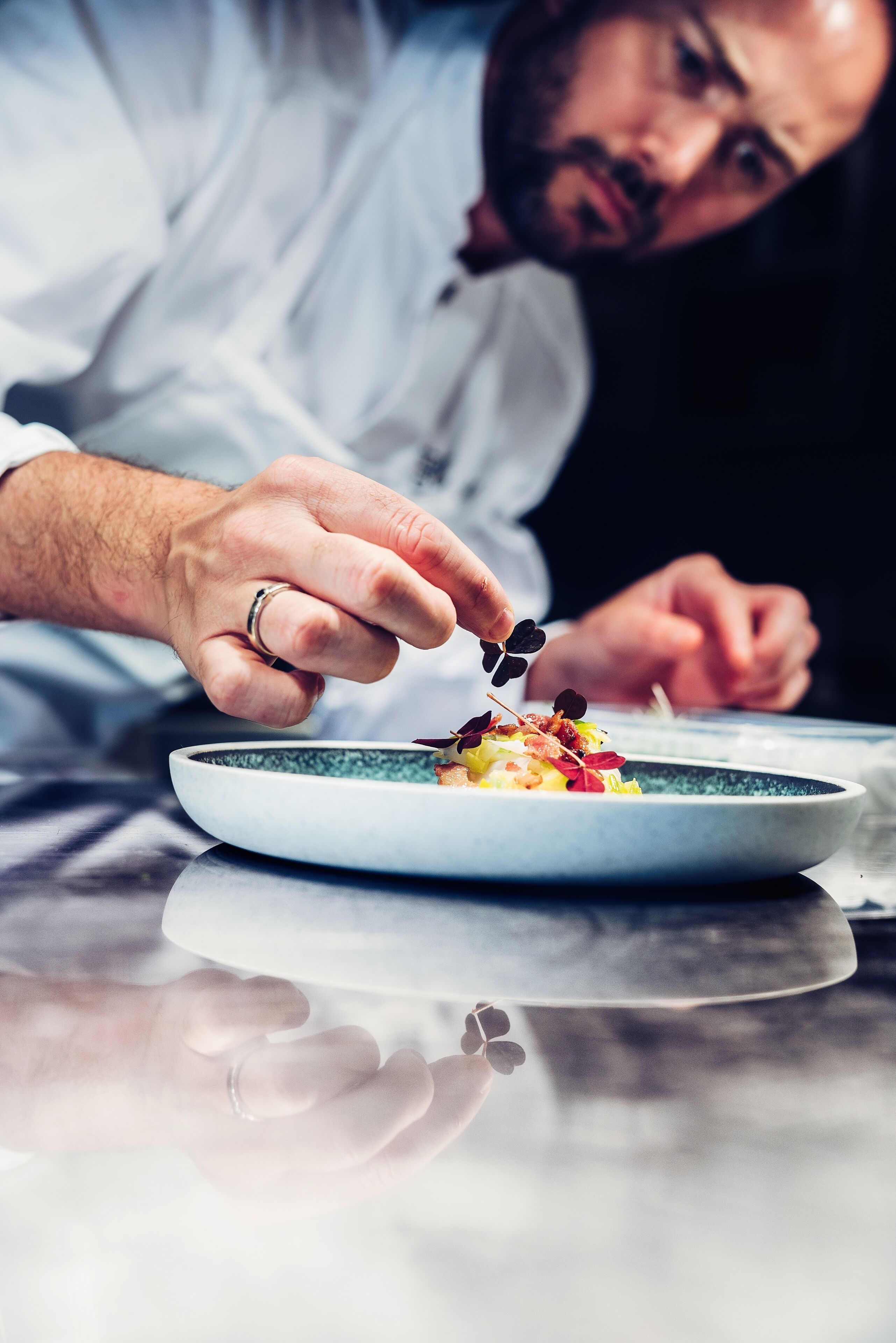 A chef's hand holding a fork, poised to eat a dish on a plate.