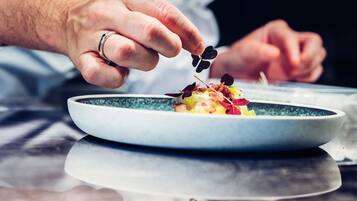 A chef's hand holding a fork, poised to eat a dish on a plate.