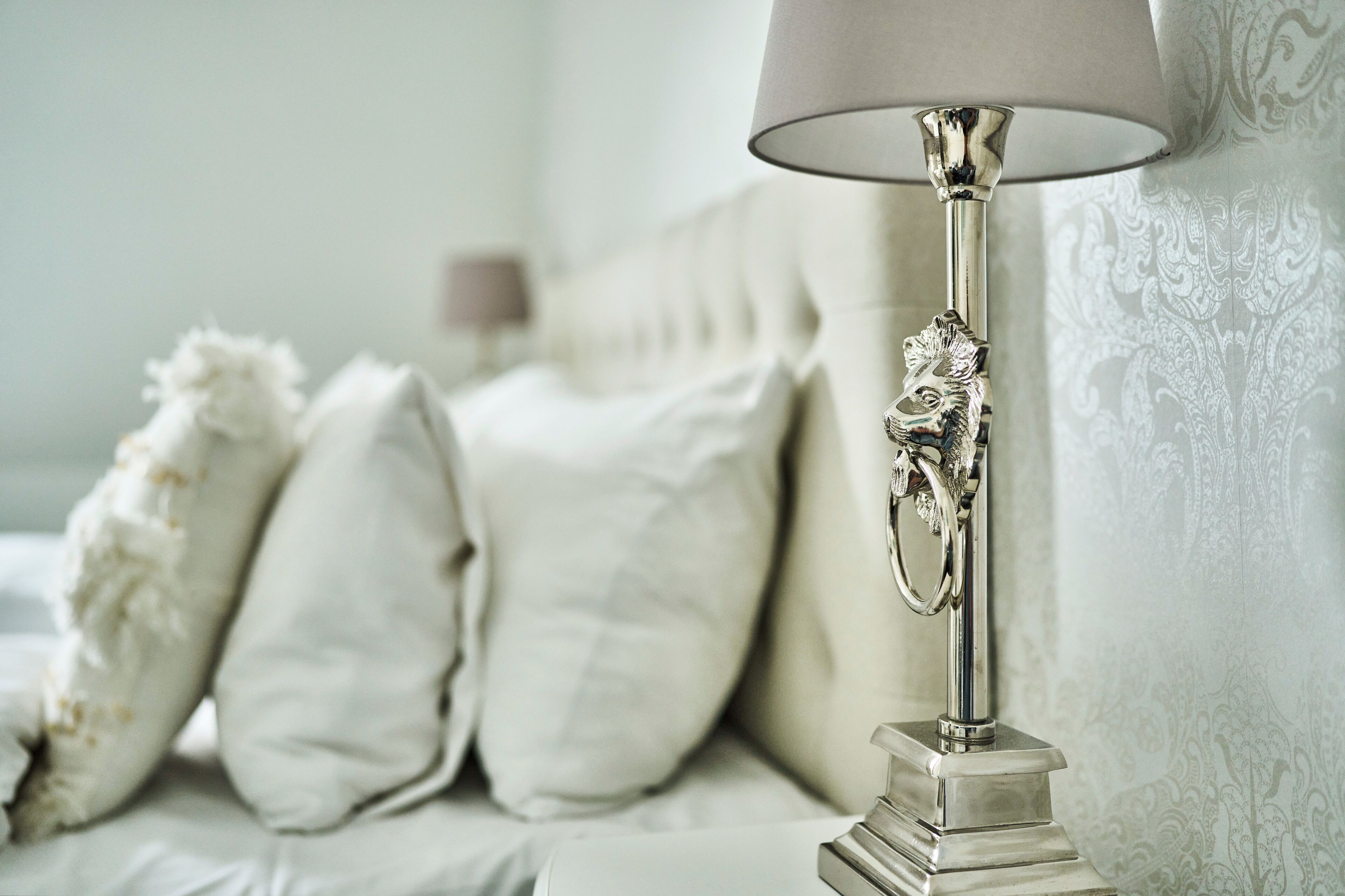 A bed with white bedding and a decorative lamp with a metallic base and a patterned lampshade.