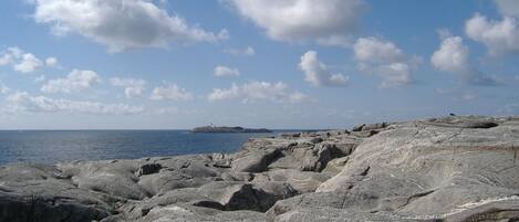 A rocky shoreline with a lighthouse in the distance under a partly cloudy sky.