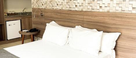 Habitación de hotel con cama, mesita de noche con teléfono, escritorio pequeño con computadora y pared con diseño geométrico.