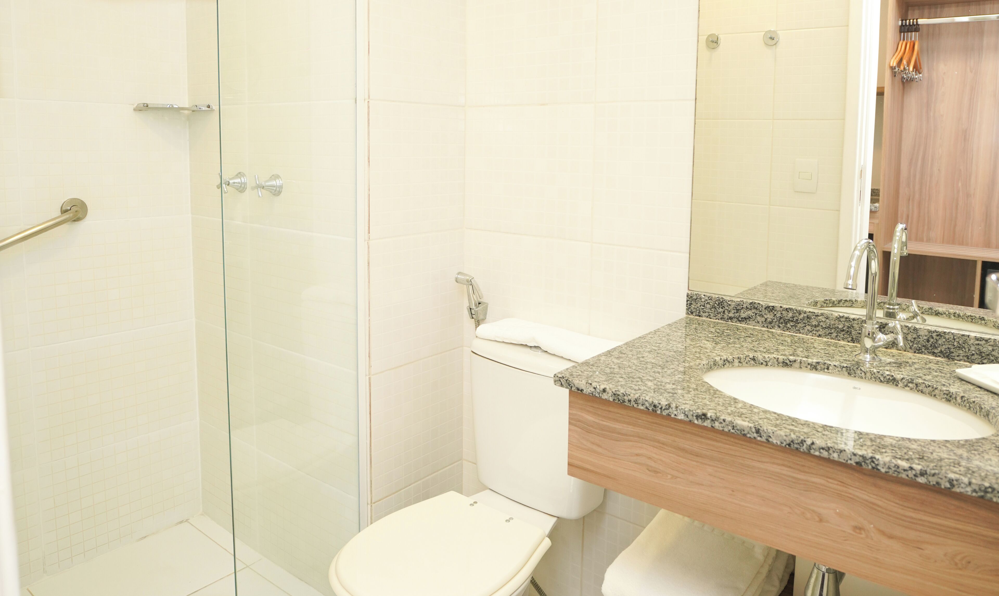 Un baño con cabina de ducha de vidrio, inodoro blanco y lavamanos con encimera de granito e instalación de tocador de madera.