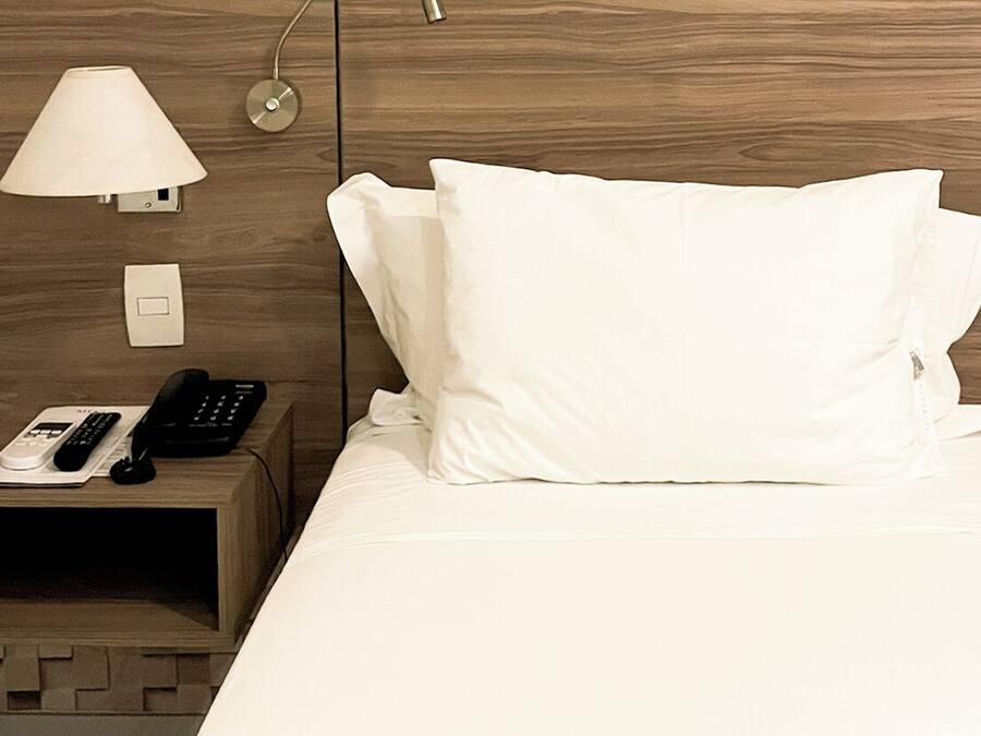 Habitación de hotel con cabecera de madera, lámpara de noche, teléfono y ropa de cama blanca.