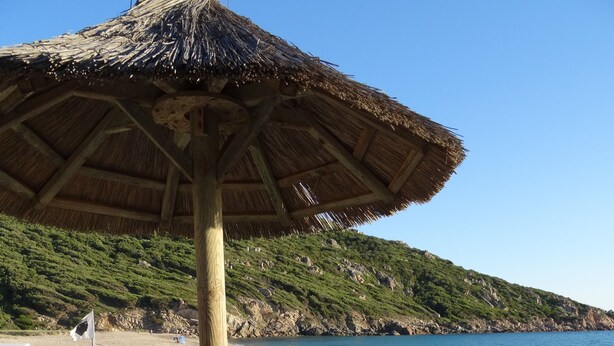 Et loungeområde ved stranden med fletningsmøbler, en stråparasol og havudsigt.