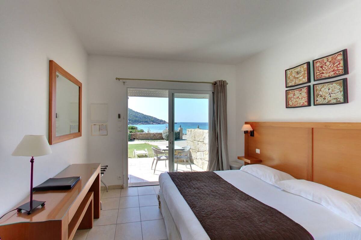 A hotel room with a bed, a desk, a chair, and a view of the sea.