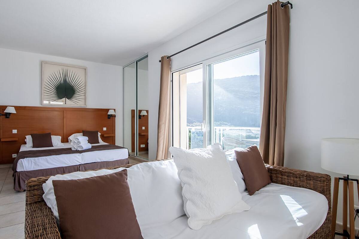 A hotel room with a large bed, a smaller bed, a view of the city, and a balcony.