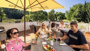 An outdoor dining area with wicker furniture, a table with a fruit platter, and a yellow umbrella. - Hotel Park (Piestany)