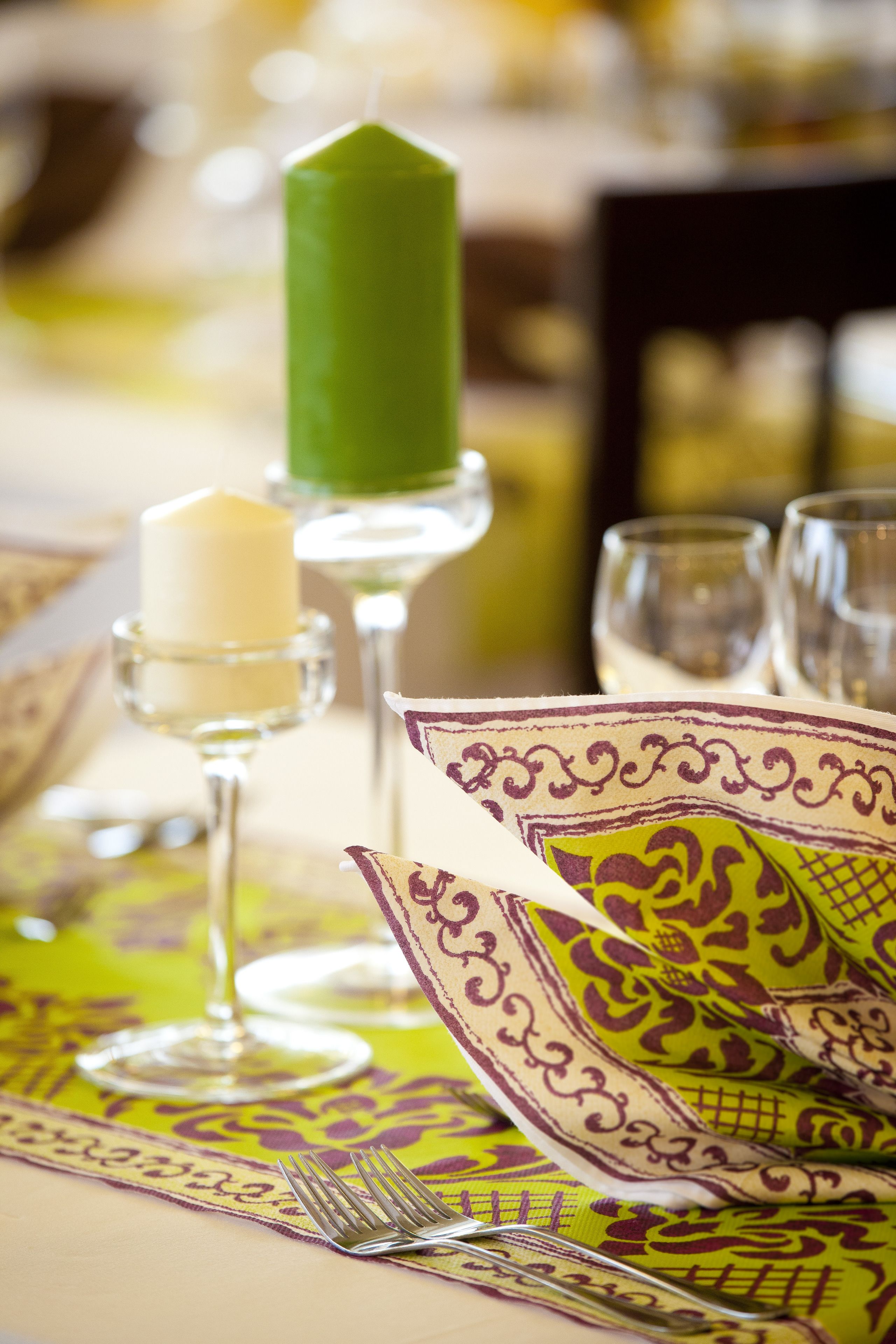 Une table dressée avec une bougie verte, une bougie blanche et un chemin de table à motifs.