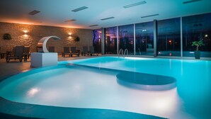 A modern indoor swimming pool with a clear view of the poolside area, including lounge chairs and a stone wall. - Hotel Park (Piestany)