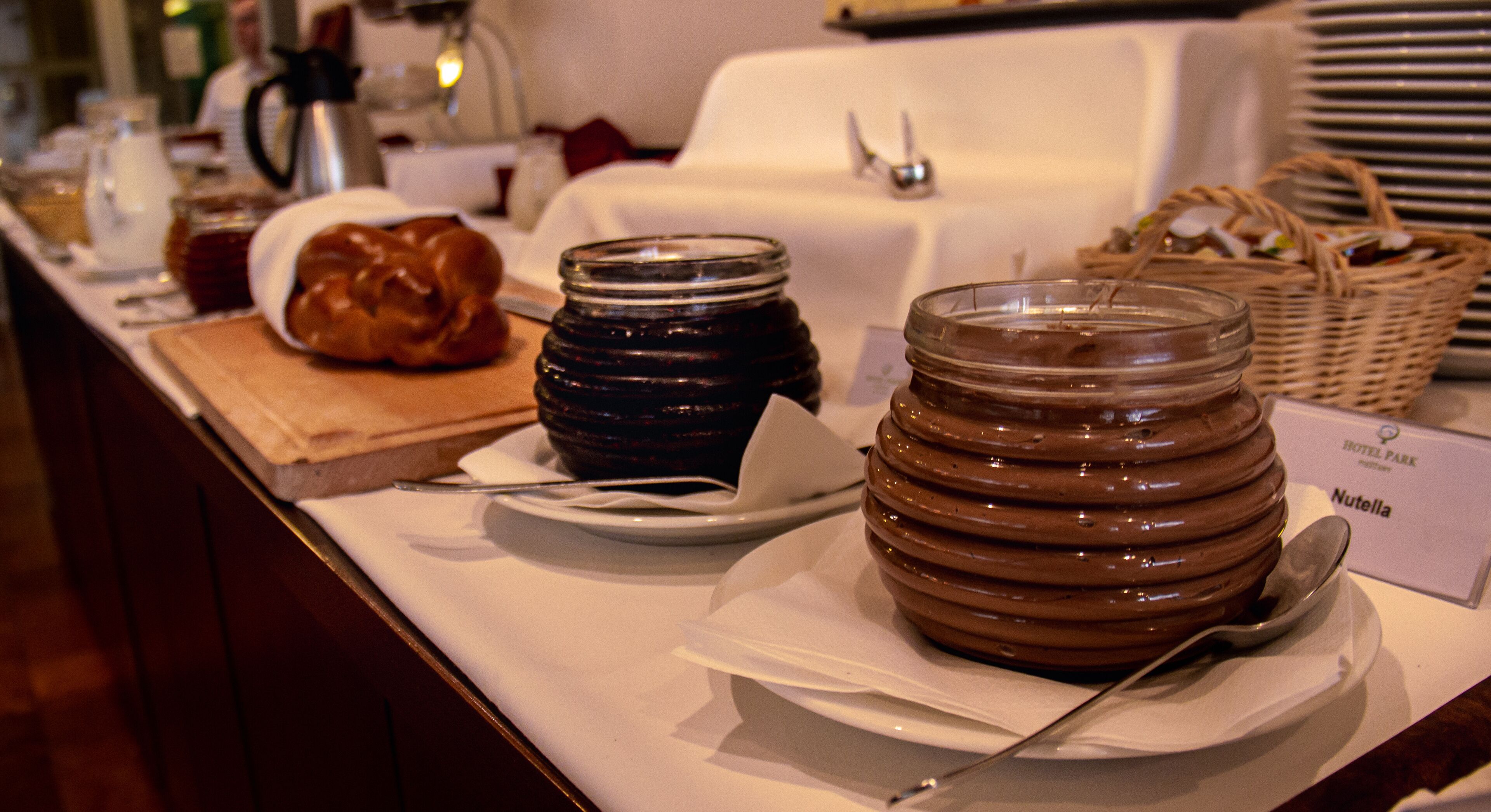 Presentación de alimentos que incluye frascos de mermelada y una hogaza de pan, con un letrero que dice 'Nutella'.