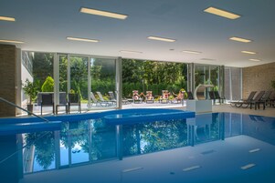 Una piscina interior con paredes de vidrio transparente, sillas de descanso y vistas al exterior.