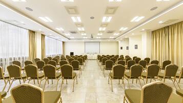 A conference room with rows of chairs, a projector screen, and a presentation area.