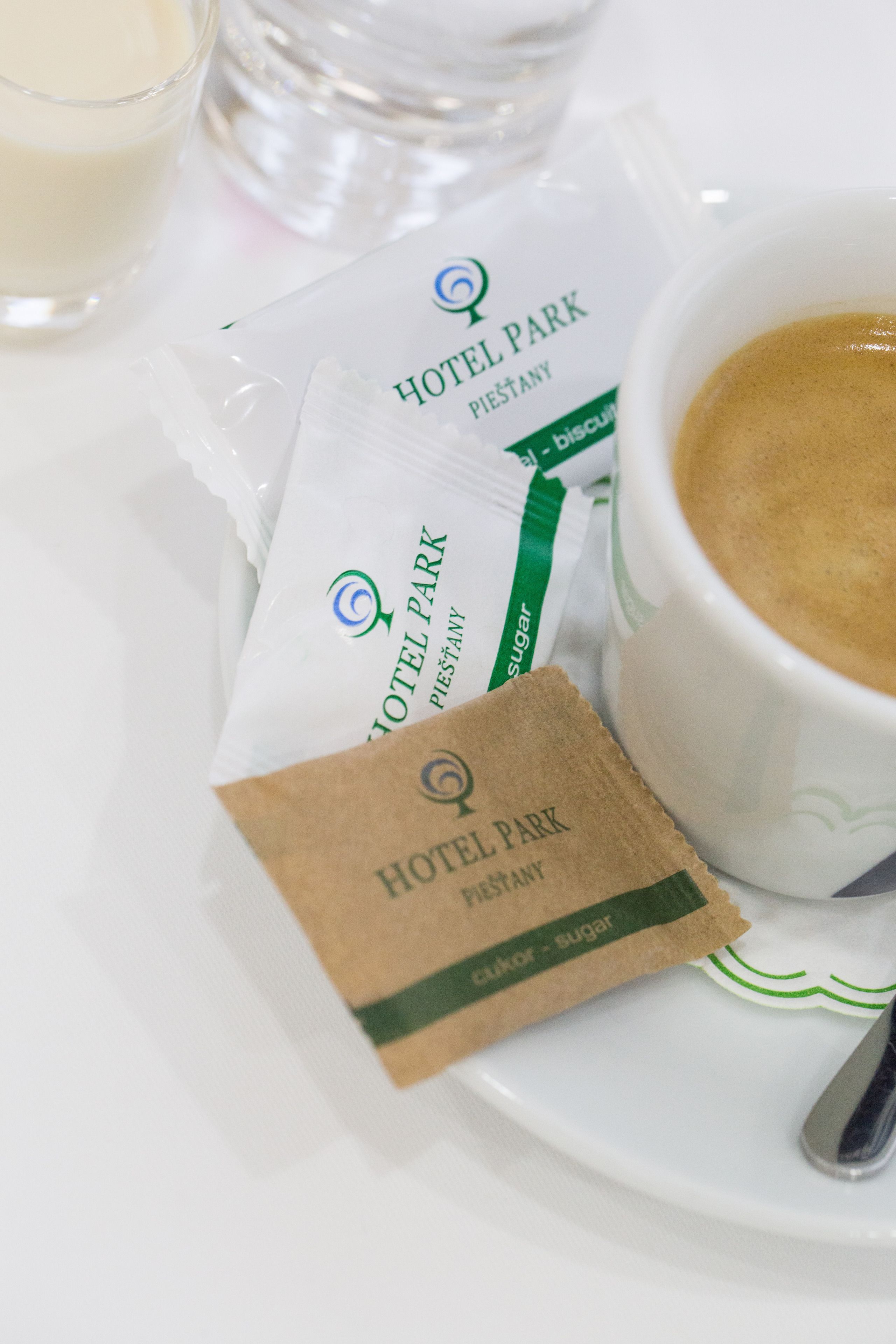 Morgenmad med en kop kaffe, et glas mælk og to sukkerpakker med teksten 'Hotel Park'.