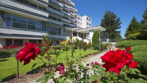 A modern hotel with a multi-story structure, a well-maintained garden with red roses, and a clear blue sky. - Hotel Park (Piestany)