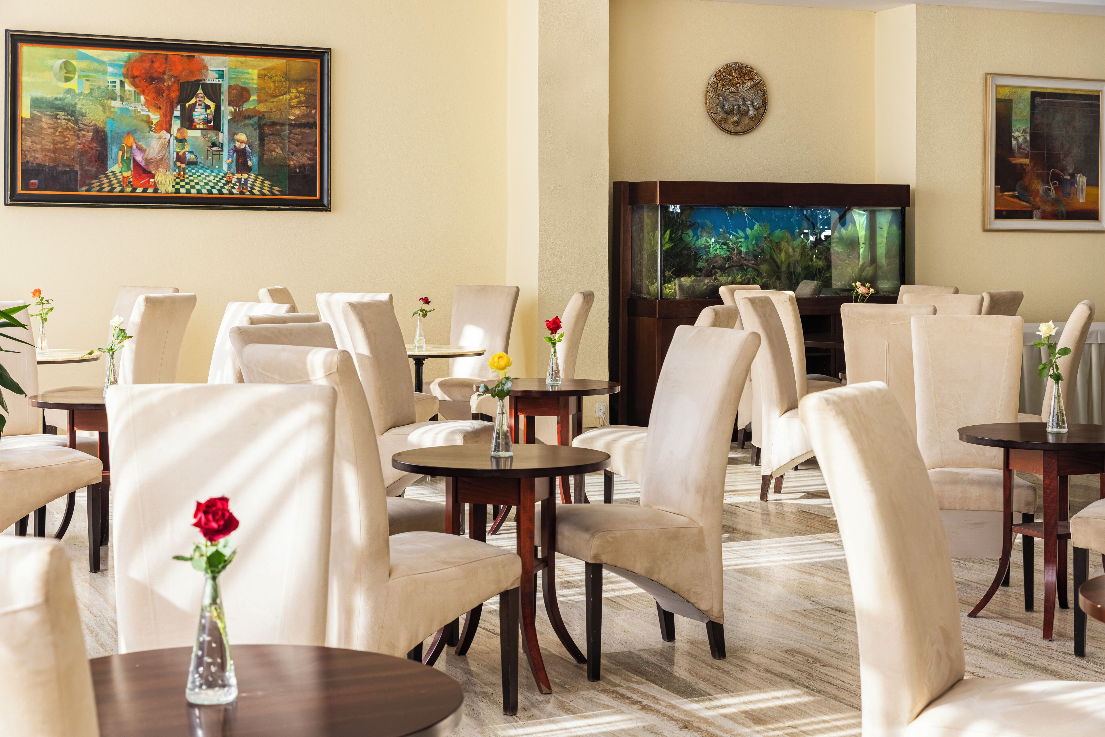 A hotel dining area with round tables, cushioned chairs, and artwork on the walls.