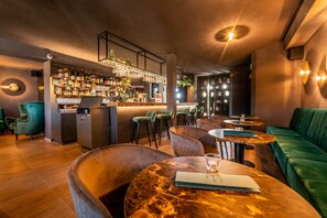 Un espace bar doté d’un comptoir en marbre, de tabourets de bar et d’un canapé recouvert d’un tissu vert.