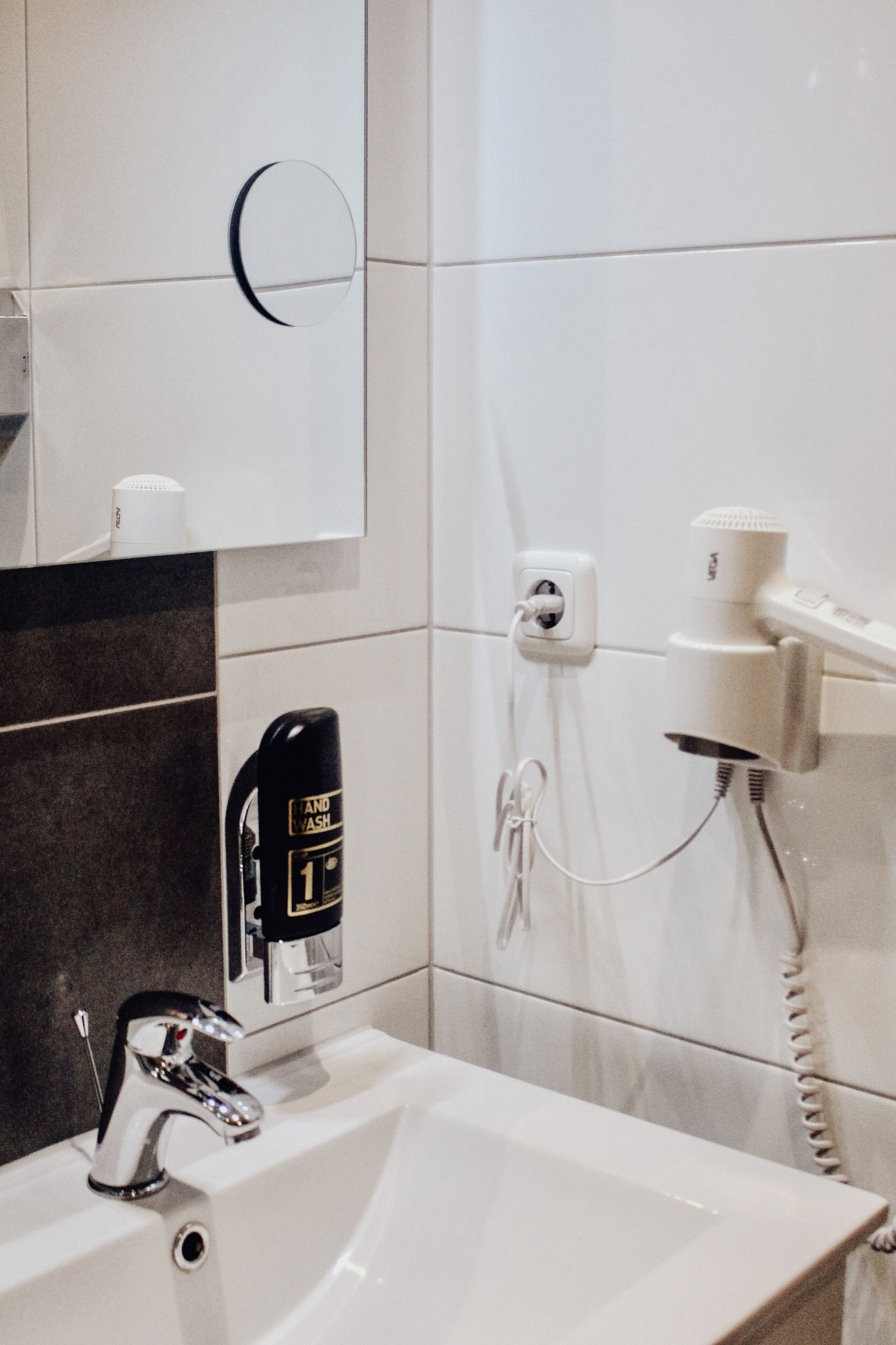 A bathroom with a sink, a hairdryer, and a hand dryer on a wall-mounted station.