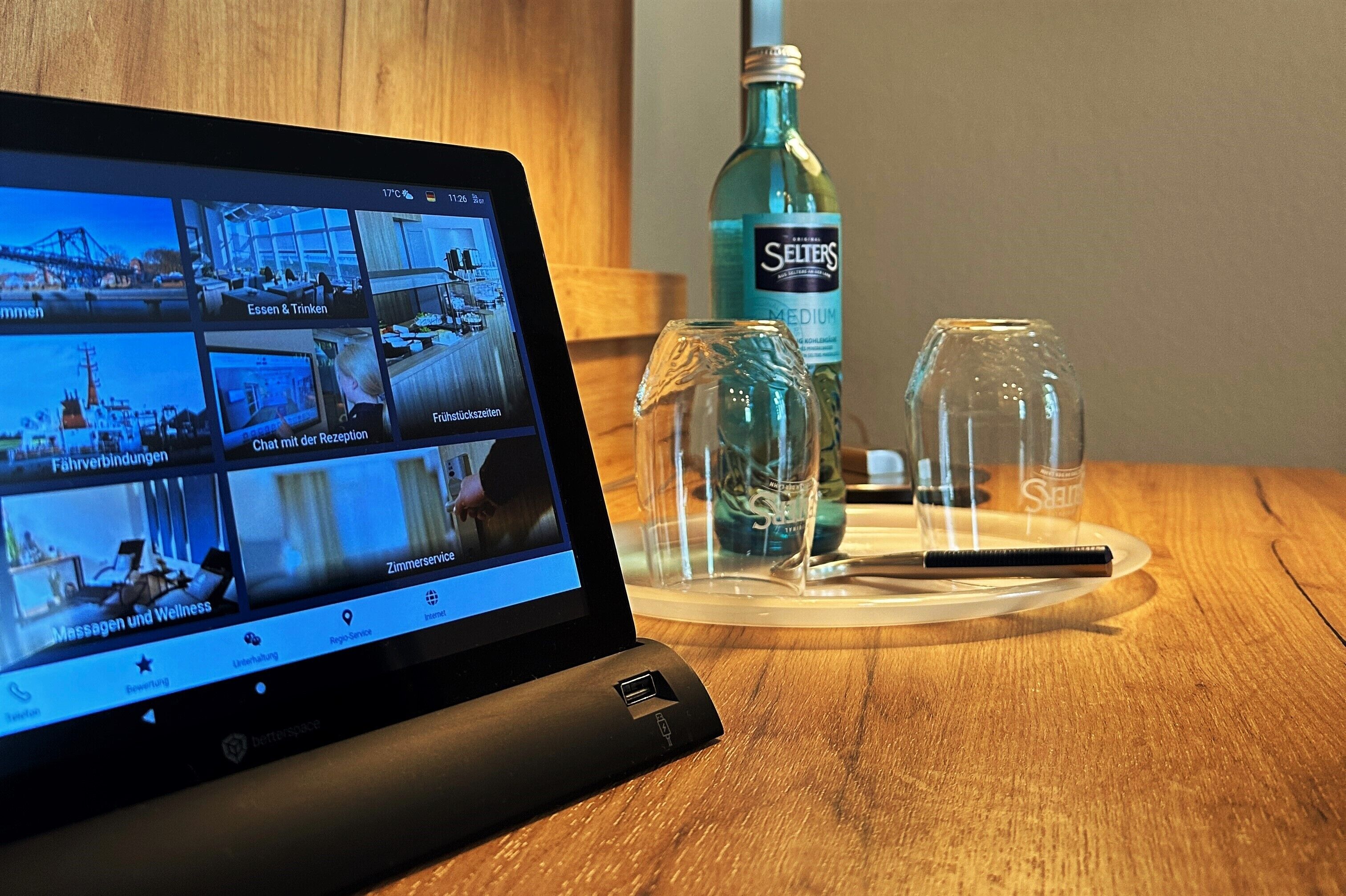 En bärbar dator som visar en virtuell rundtur i ett hotellrum, med bekvämligheter som en minibar, ett glas vatten och en penna på en underlägg.