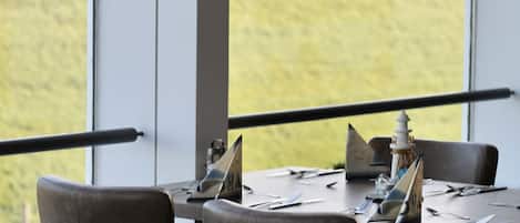 A dining area with tables set for two, large windows offering a view of the sea, and a railing along the window.