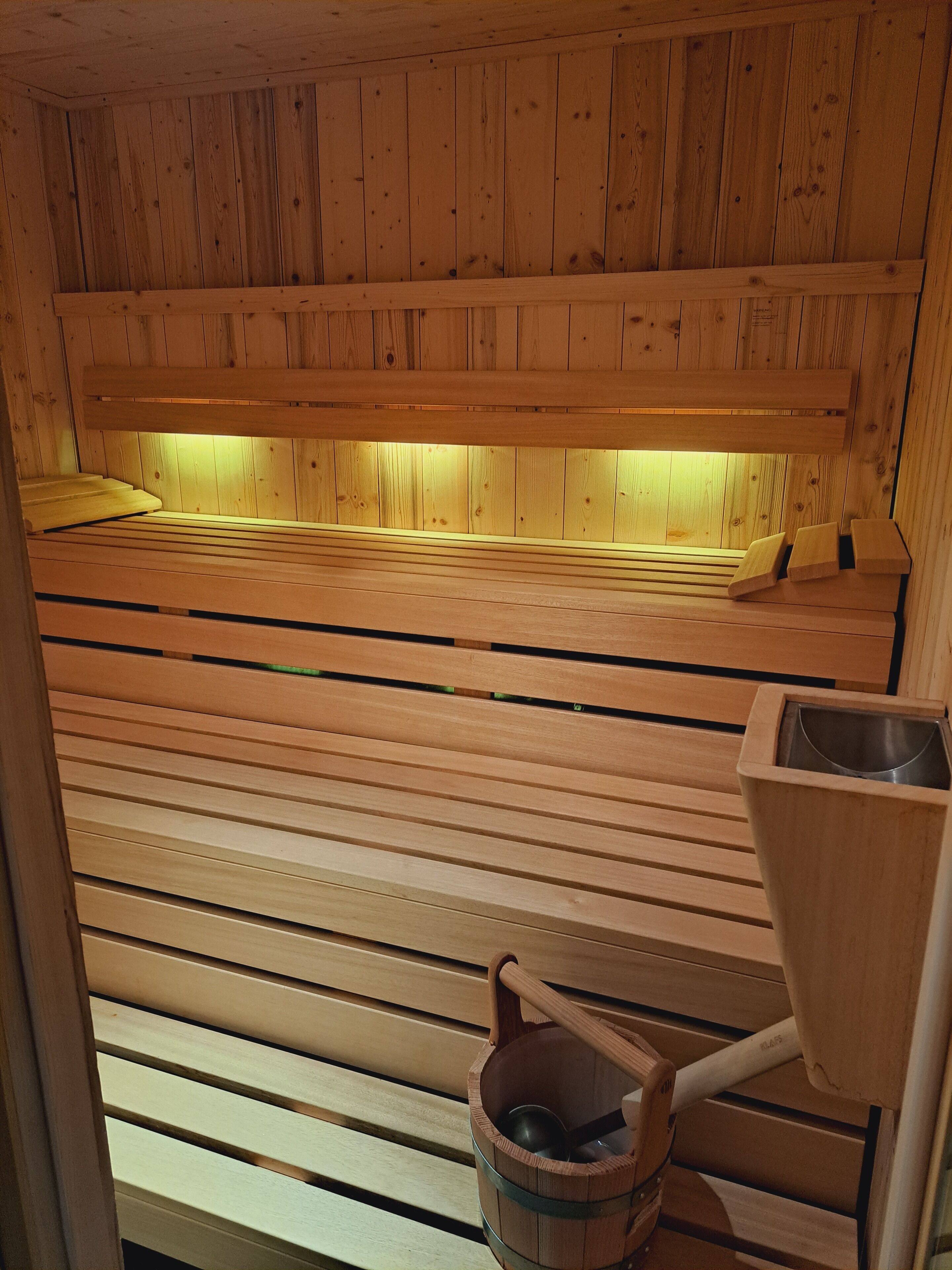 Un sauna en bois, avec des bancs et un seau en bois accompagné d’une louche.
