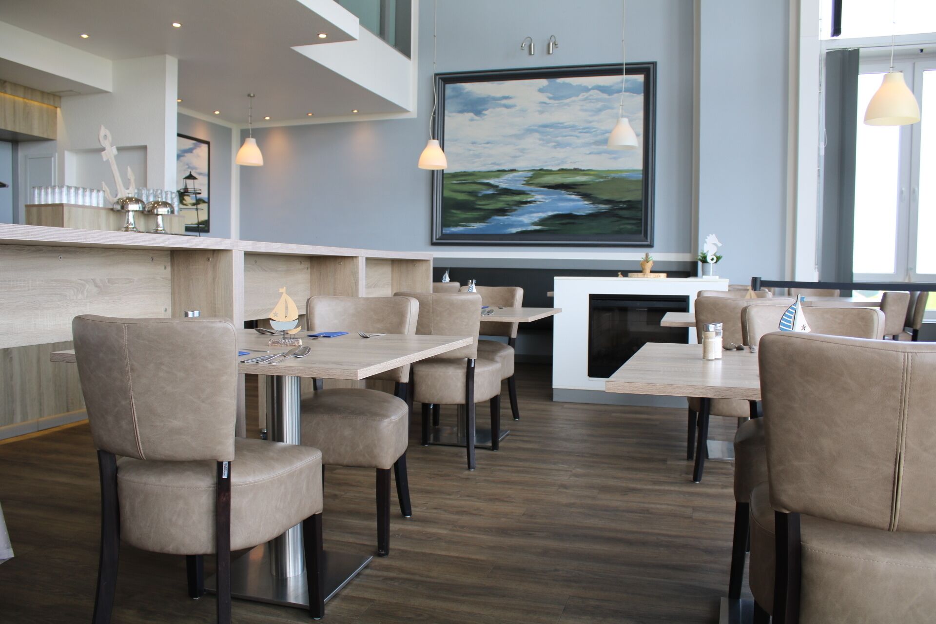 A modern restaurant with high tables and chairs, a fireplace, and a large painting of a landscape.