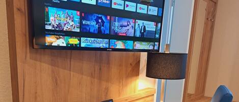 A modern living room with a flat-screen TV mounted on the wall displaying various streaming apps.