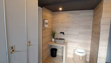 A modern bathroom with a wooden wall, a sink, a toilet, and a black trash bin.
